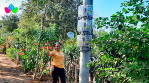 Joven saludando a la par de un medidor de energía eléctrica ubicados en un poste de la comunidad La Montañita de Tisma, Masaya.