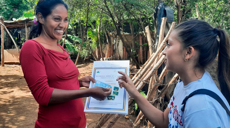 Habitante de la comarca El Portillo en el municipio de Nindirí, departamento de Masaya, recibiendo su titulo de propiedad de manos de una joven miembro de Promotoría Solidaria de la Juventud Sandinista.