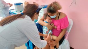 Niño en brazos de su madre siendo vacunado contra la COVID-19 por una enfermera del Ministerio de Salud de Nicaragua.