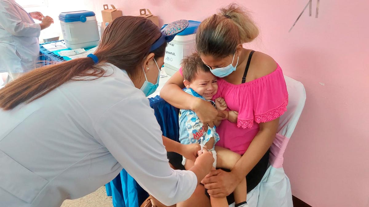 Niño en brazos de su madre siendo vacunado contra la COVID-19 por una enfermera del Ministerio de Salud de Nicaragua.