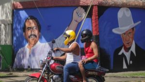 Motociclista y pasajero pasan frente a un mural de Sandino y el Comandante Daniel