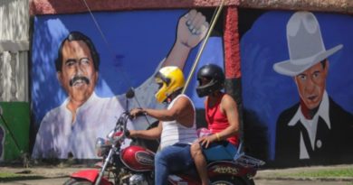 Motociclista y pasajero pasan frente a un mural de Sandino y el Comandante Daniel