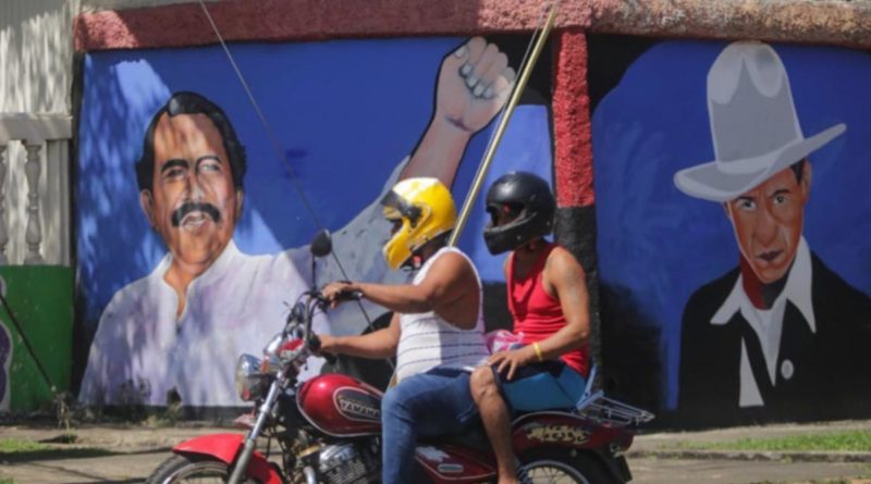 Motociclista y pasajero pasan frente a un mural de Sandino y el Comandante Daniel