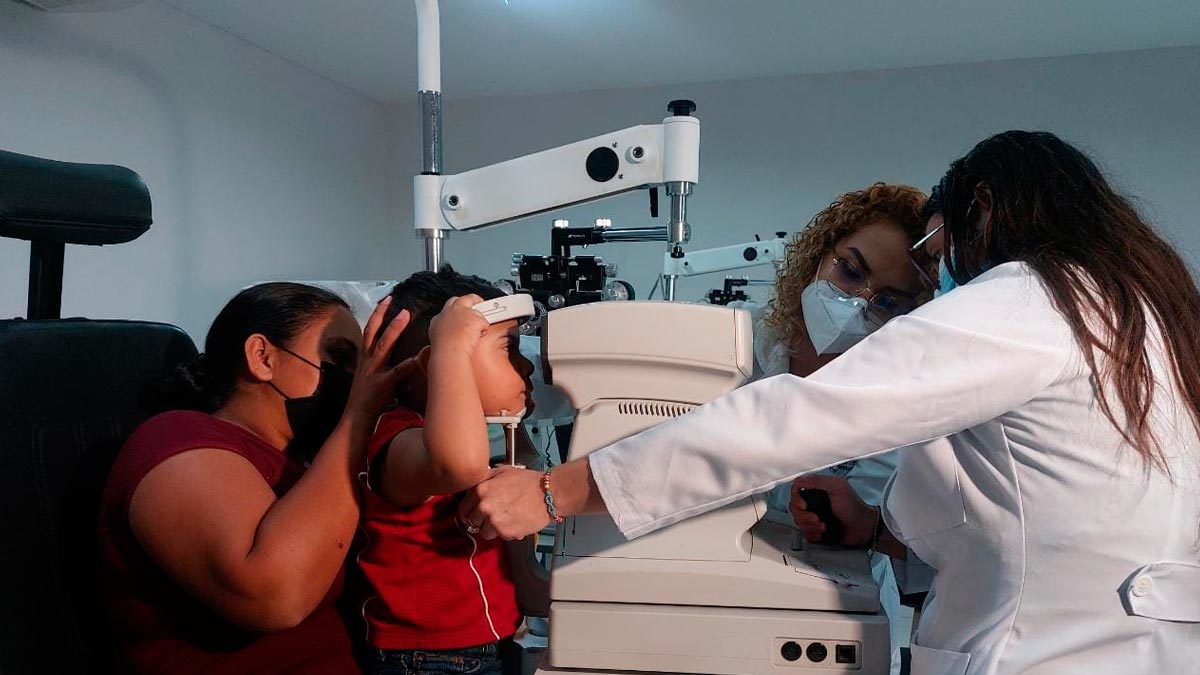 Médico del Centro Nacional de Oftalmología (CENAO), realizando examen visual a una niña acompañada por su madre.