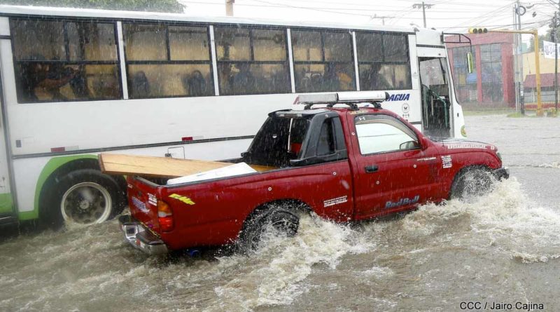 Dos vehículos pasan por una calle mientras llueve en Managua