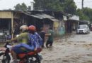 Motociclistas y jóvenes atravesando una calle mientras llueve en Managua