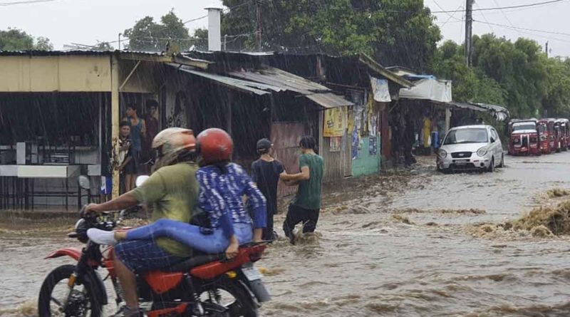 Motociclistas y jóvenes atravesando una calle mientras llueve en Managua