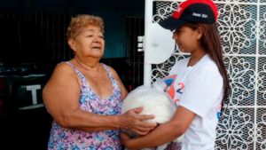 Miembro de Promotoría Solidaria de la Juventud Sandinista 19 de Julio, entregando paquete alimenticio a madre de héroe y mártir de Managua.